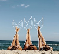 three women laying on the beach with mermaid tails drawn on their legs