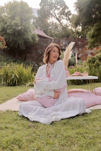 a woman in a pink robe sitting on a blanket in a garden