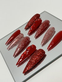 a group of red glitter nails on a mirror