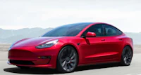 the red tesla model 3 is driving down the road