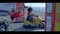 two girls riding a toy motorbike on a pier