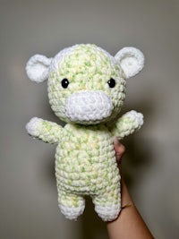 a person holding a crocheted green and white stuffed animal