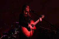 a woman playing an acoustic guitar in front of a microphone
