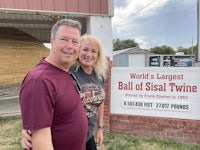 a man and woman standing in front of a sign that says world's largest ball of stale twine