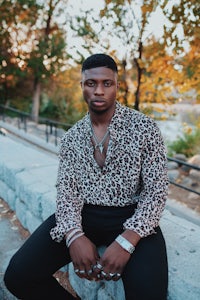 a black man in a leopard print shirt sitting on a stone wall