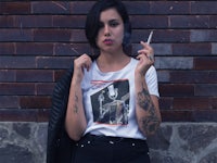 a woman smoking a cigarette in front of a brick wall