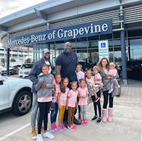 a group of children posing in front of a mercedes benz dealership