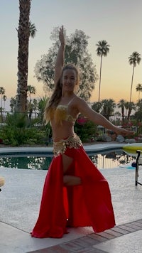 a woman in a red belly dance dress is doing a pose in front of a pool
