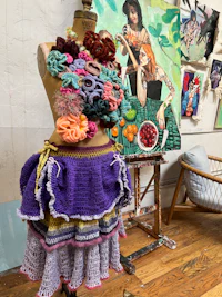 a crocheted mannequin sitting on a chair in a studio
