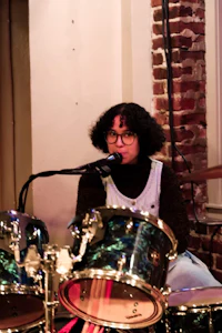 a woman playing drums in front of a brick wall