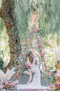 a bride in a white dress poses in front of a teepee