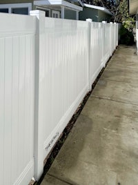 a white vinyl fence on a sidewalk next to a house