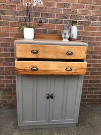 a grey dresser with two drawers and a potted plant