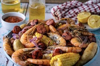 a bowl full of shrimp, corn, potatoes and beer