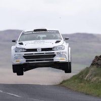 a volkswagen rally car in the air over a hill