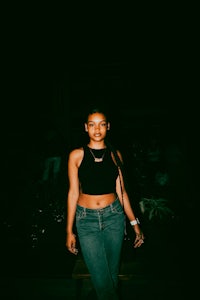 a woman in a black top and jeans standing in a dark room