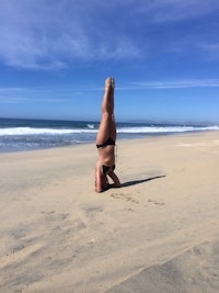 a woman doing a handstand on the beach