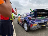 a group of people are taking pictures of a rally car