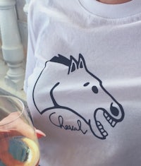 a woman holding a glass of wine and a t - shirt with a horse head on it