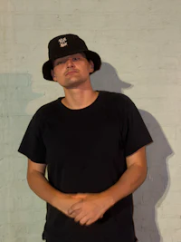 a man in a black hat standing against a brick wall