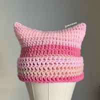 a pink crocheted cat hat on a mannequin