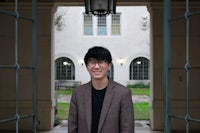 a young man in glasses standing in front of a building