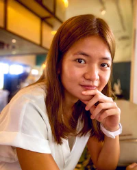 a young asian woman sitting at a table with her hand on her chin