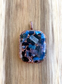a blue and copper square pendant on a wooden table