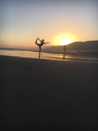 a woman doing yoga on the beach at sunset