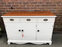 a white sideboard with wooden drawers in front of a brick wall