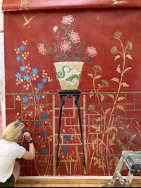 a woman is painting a red wall with a vase of flowers