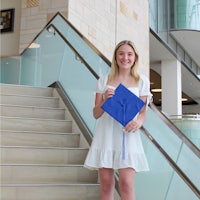a woman in a white dress standing on stairs holding a blue graduation cap
