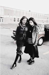 two women standing next to each other in front of a car