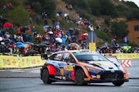 a rally car driving down a hill in front of a crowd