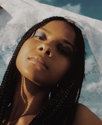 a woman with braided hair posing under a cloud