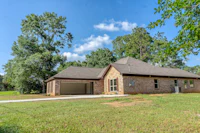 a brick home in the middle of a grassy field