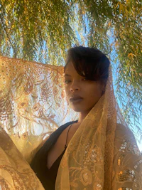a woman wearing a gold shawl in front of a tree