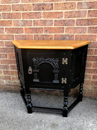 a black cabinet with a wooden top in front of a brick wall