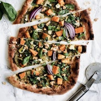 a slice of pizza with greens and onions on it