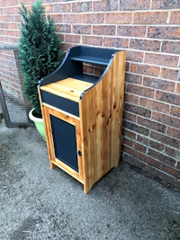 a small wooden cabinet with a black door in front of a brick wall