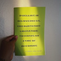 a person holding a book with the words, dwelling in believability, liberation towards an ethic of becoming