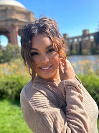 a woman in a tan sweater posing in front of a fountain