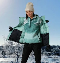 a woman in a green jacket standing next to a frozen lake