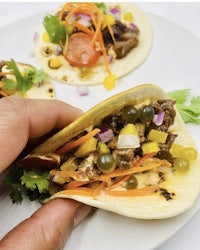 a person holding up two tacos on a plate