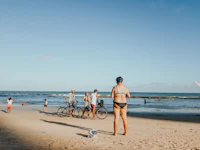 a woman in a bikini is standing on the beach with her bike