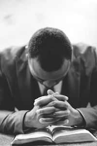 a black man in a suit praying with his hands on his knees