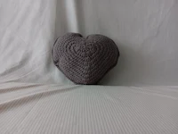 a heart shaped crocheted pillow sitting on top of a white sheet