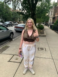 a woman in a crop top and sweatpants standing on a sidewalk