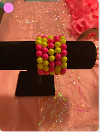 a pink and yellow beaded bracelet on a black stand