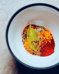 a bowl of spices with a leaf in it
